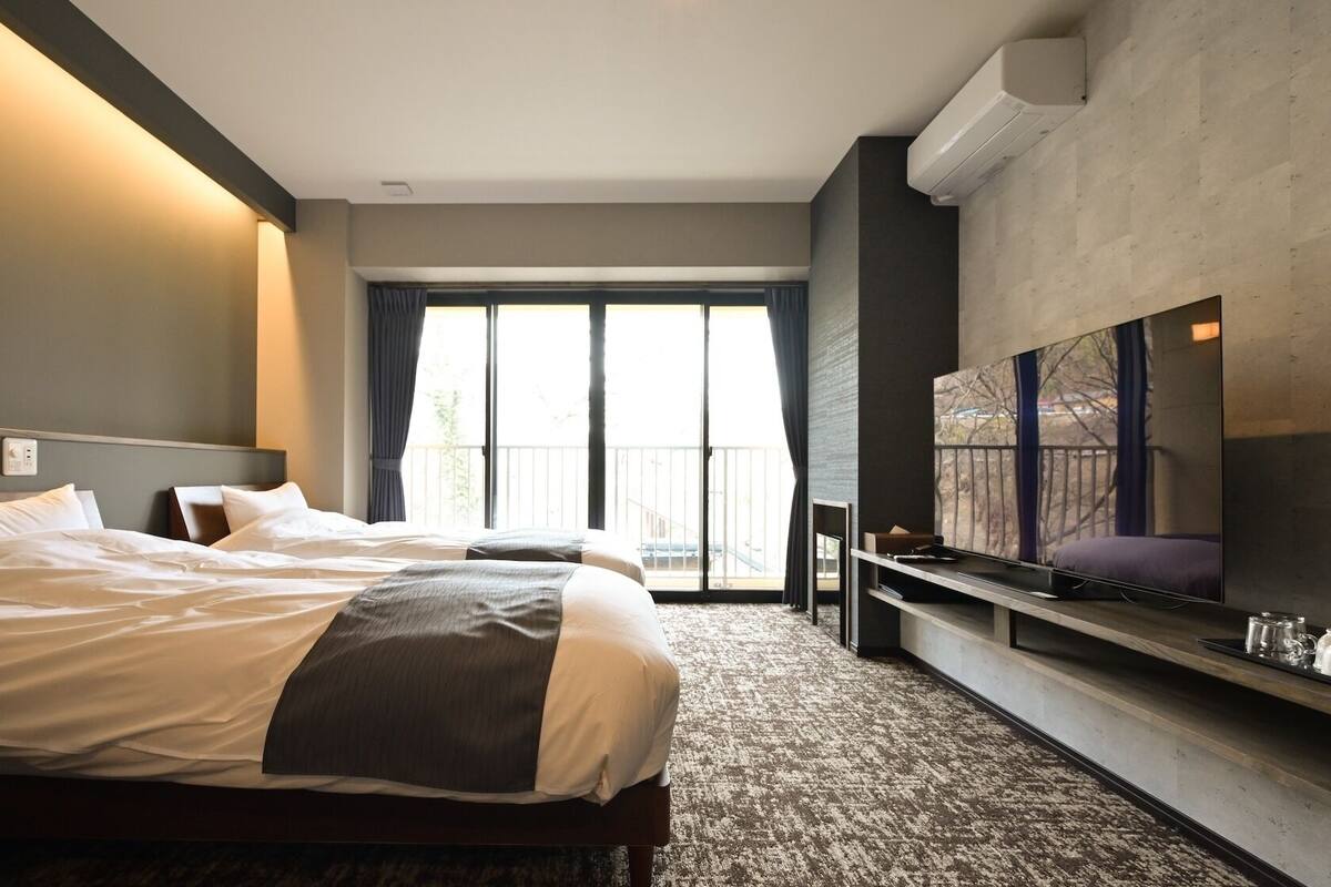 Ein Hotelzimmer mit einem großen Bett, einem flachbildfernseher an der Wand und einem Balkon mit Blick.