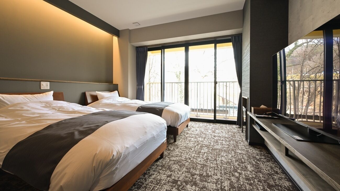 A hotel room with two beds, a large window, and a flat-screen TV.