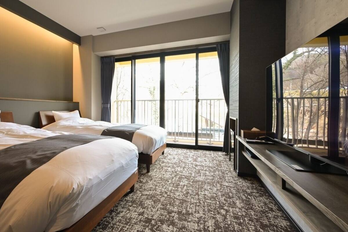 Ein Hotelzimmer mit zwei Betten, einem großen Fenster und einem Flachbildfernseher.