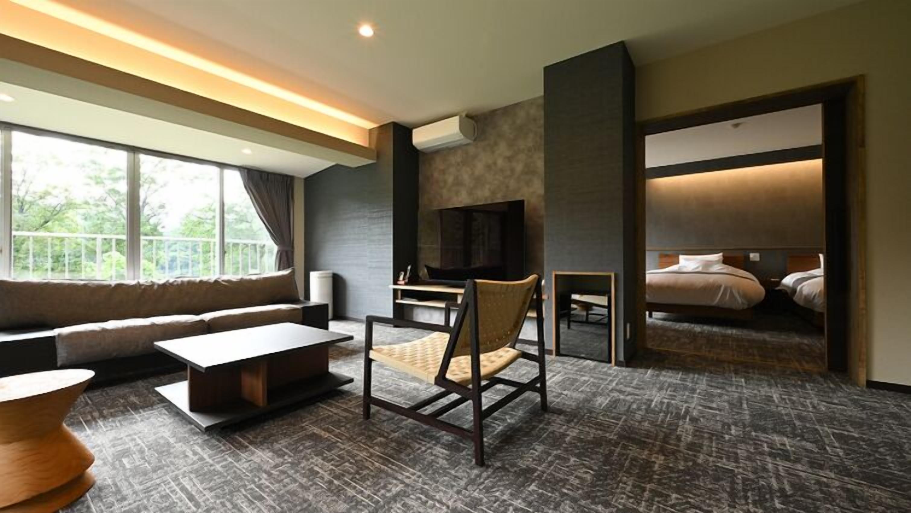 A modern hotel room with a sofa, a small table, a chair, a TV, and a bed.