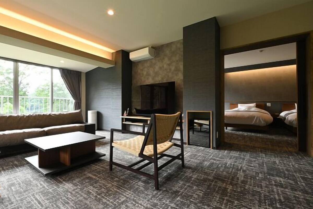 Ein modernes Hotelzimmer mit einer Couch, einem kleinen Tisch, einem Sessel, einem Fernseher und einem Bett.