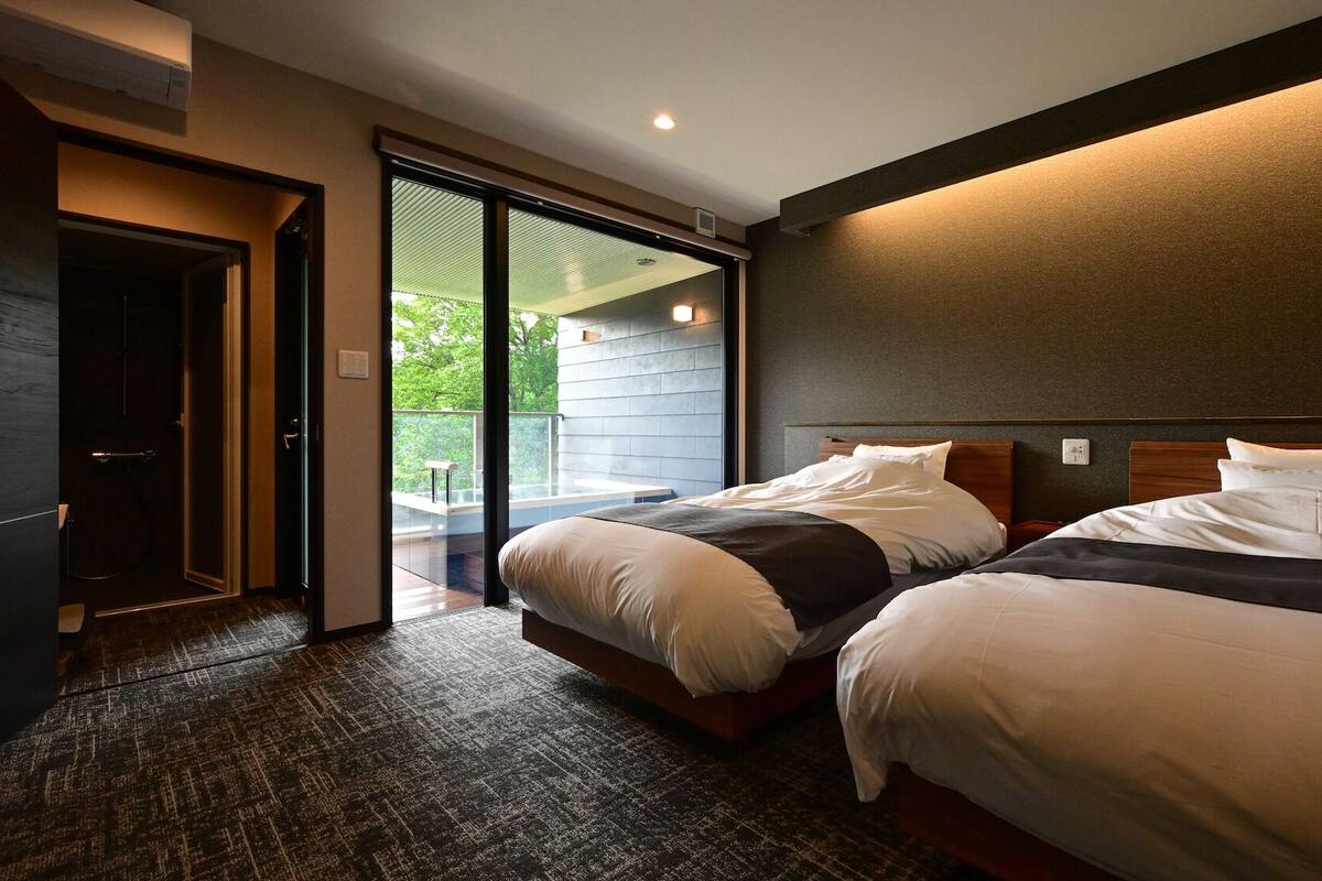 Ein Hotelzimmer mit zwei Betten, einer Schiebetür zu einem Balkon und einem dunklen Teppichboden.