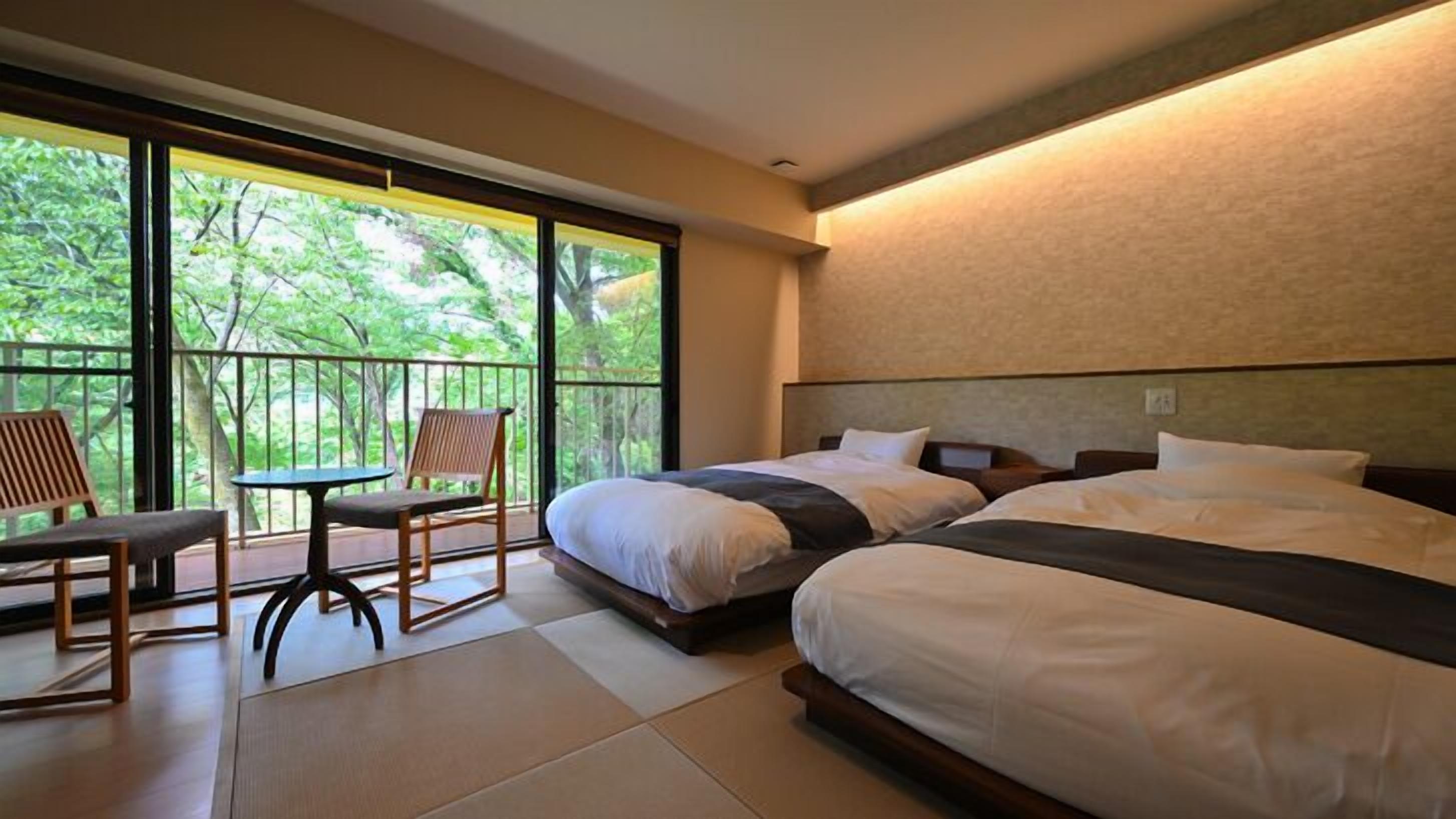 Ein Hotelzimmer mit zwei Betten, einem Balkon mit Tisch und Stühlen sowie großen Fenstern.