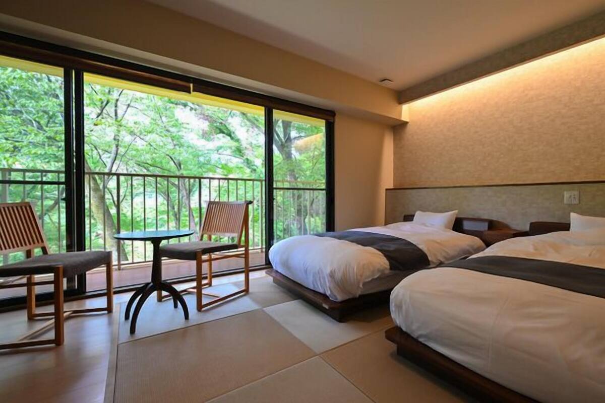 Ein Hotelzimmer mit zwei Betten, einem Balkon mit Tisch und Stühlen sowie großen Fenstern.