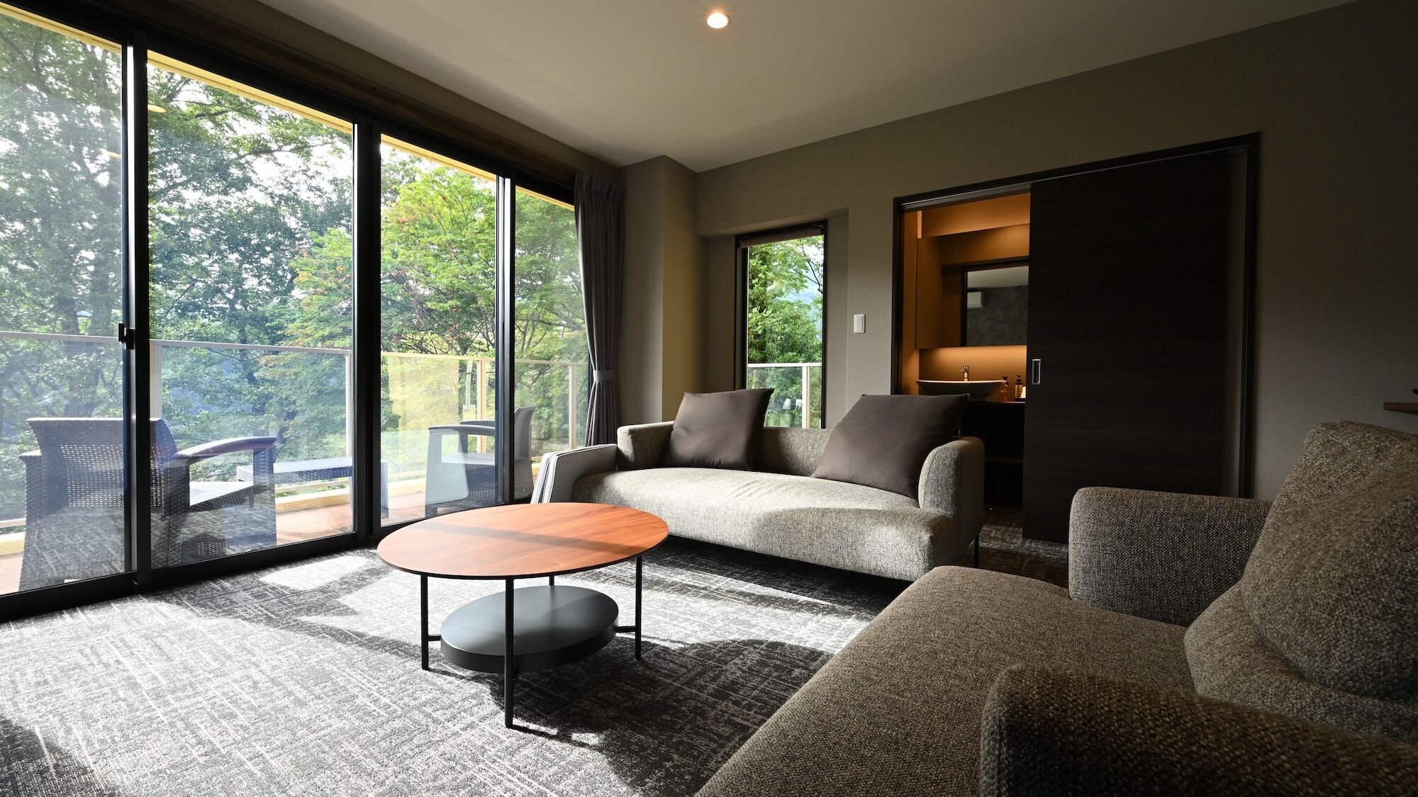 Ein modernes Wohnzimmer mit einer Couch, einem runden Couchtisch und Blick auf einen Balkon mit Gartenmöbeln.