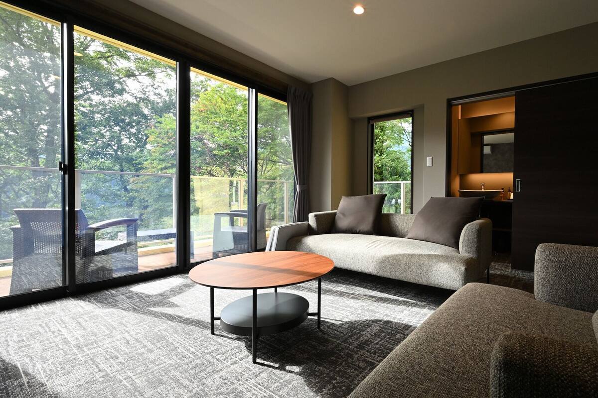 Ein modernes Wohnzimmer mit einer Couch, einem runden Couchtisch und Blick auf einen Balkon mit Gartenmöbeln.