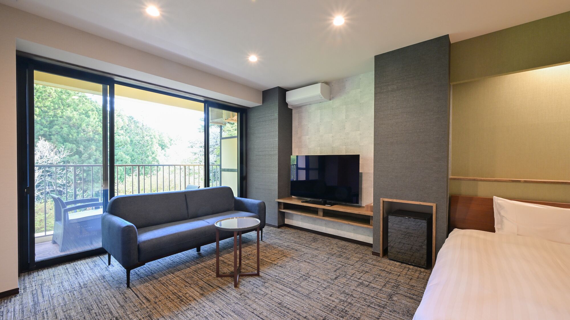 Ein modernes Hotelzimmer mit einer Couch, einem kleinen Tisch, einem Fernseher und einem Bett.