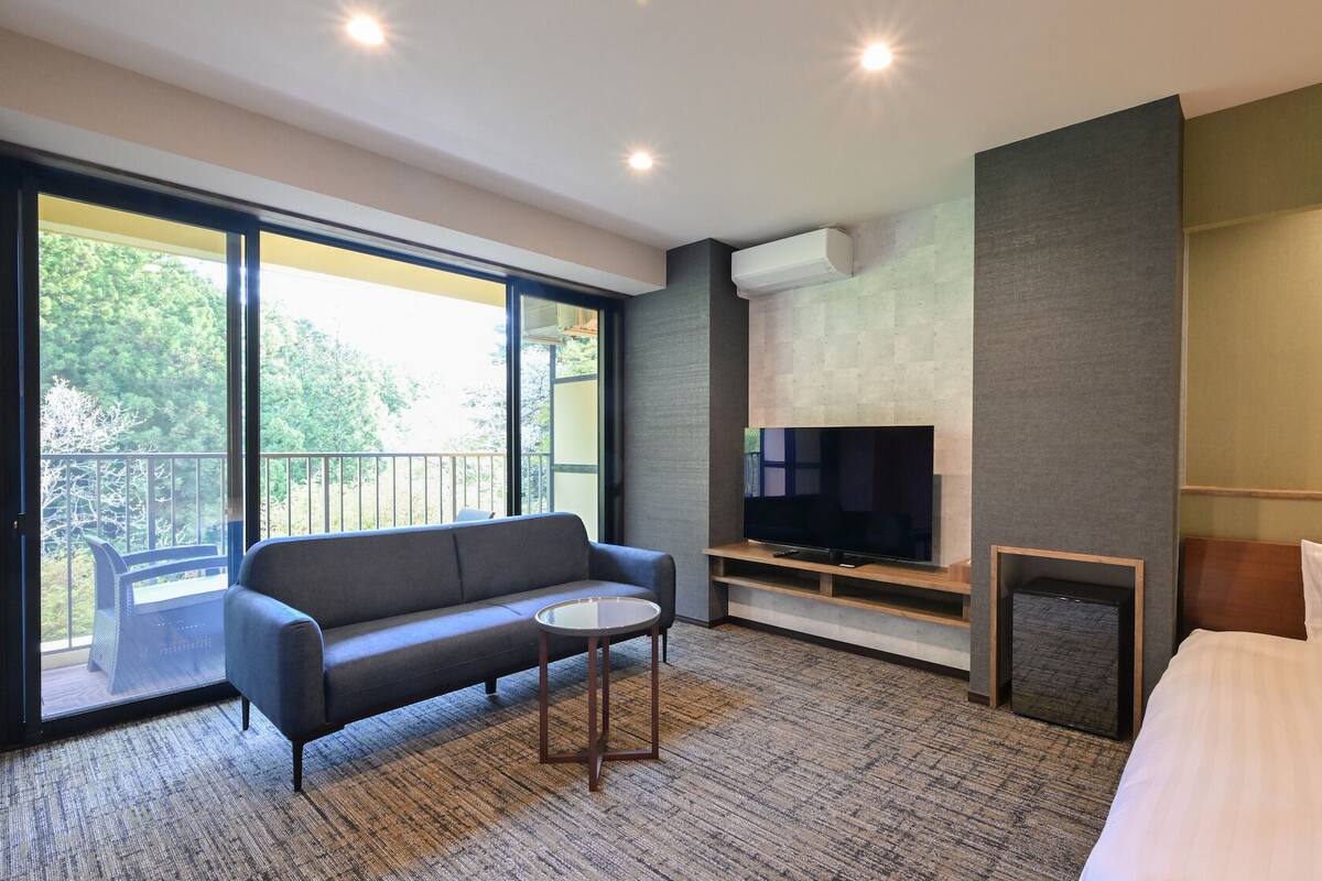 Ein modernes Hotelzimmer mit einer Couch, einem kleinen Tisch, einem Fernseher und einem Bett.