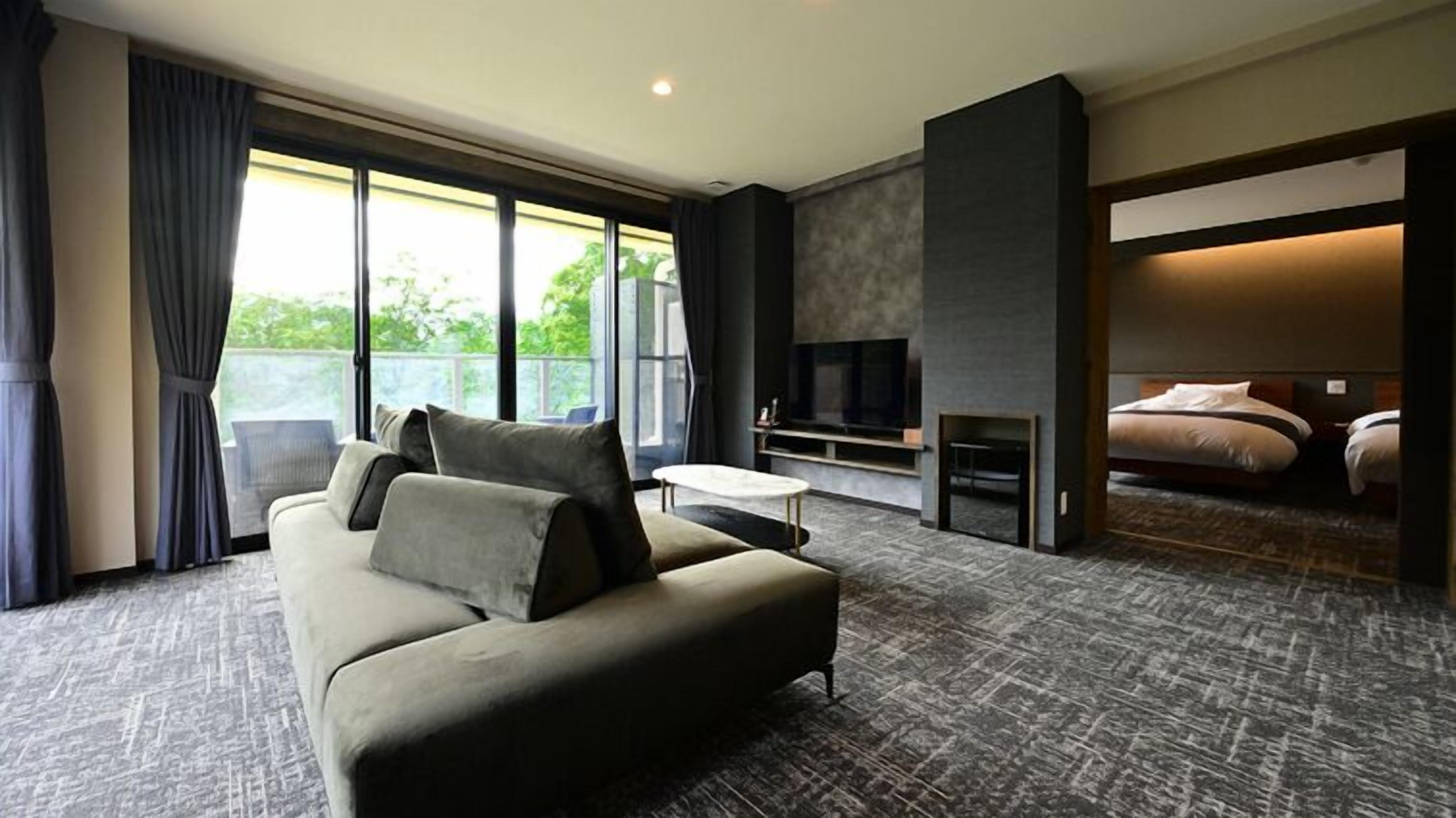 A modern hotel room with a sofa, TV, fireplace, and a balcony view.