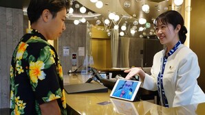 A reception area with a polished counter, a digital tablet, and a person interacting with it. - Quintessa Hotel Tokyo Haneda Comic & Books (Tokyo)