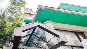 The exterior of the Mitaka City Hotel with a modern geometric entrance and a green awning. - Mitaka City Hotel (Mitaka)