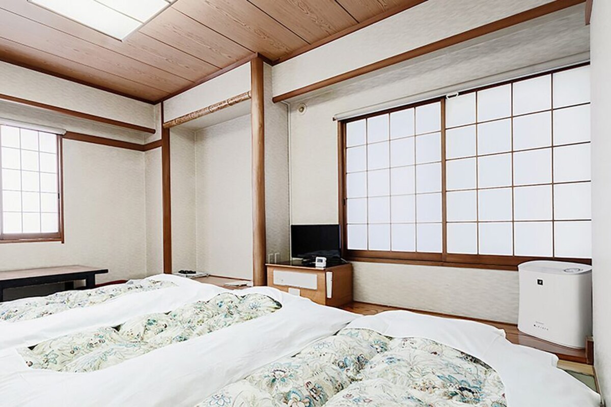 A room with two beds, a TV, a heater, and large windows.