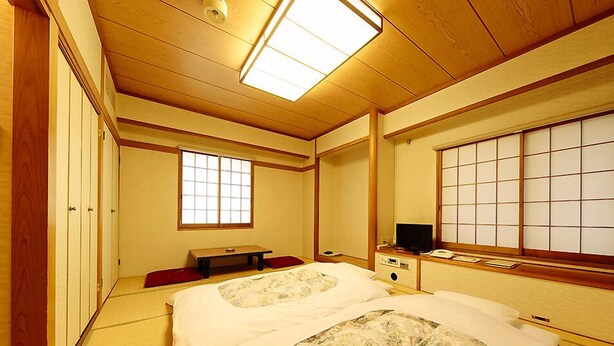 A traditional Japanese-style room with tatami flooring, a futon bed, sliding doors, and a television. - Mitaka City Hotel (Mitaka)