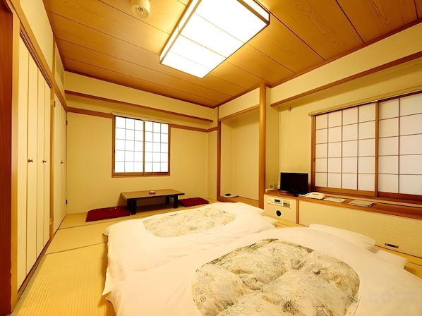 A traditional Japanese-style room with tatami flooring, a futon bed, a television, and sliding doors. - Mitaka City Hotel (Mitaka)