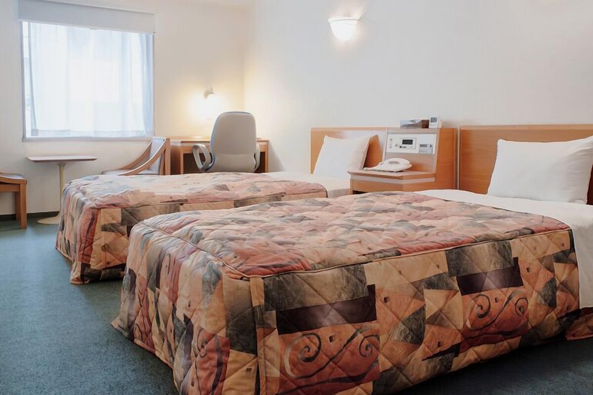 A hotel room with two beds, a desk, a chair, and a bedside table with a phone.