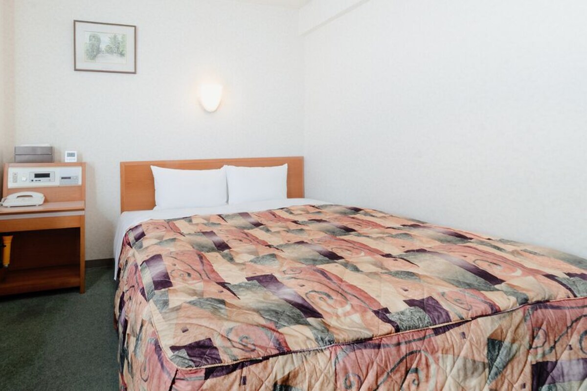 A hotel room with a bed, a desk with a telephone, and a chair.