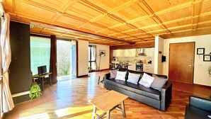 A spacious living area with a wooden ceiling, a sofa with cushions, a wooden coffee table, and a kitchen in the background.