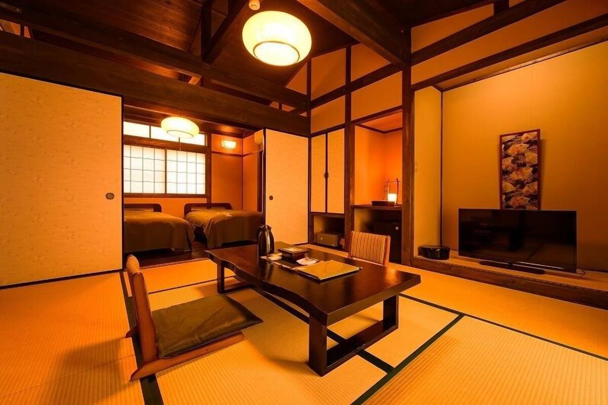 A traditional Japanese room with tatami flooring, a low table, cushions, a television, and sliding doors.