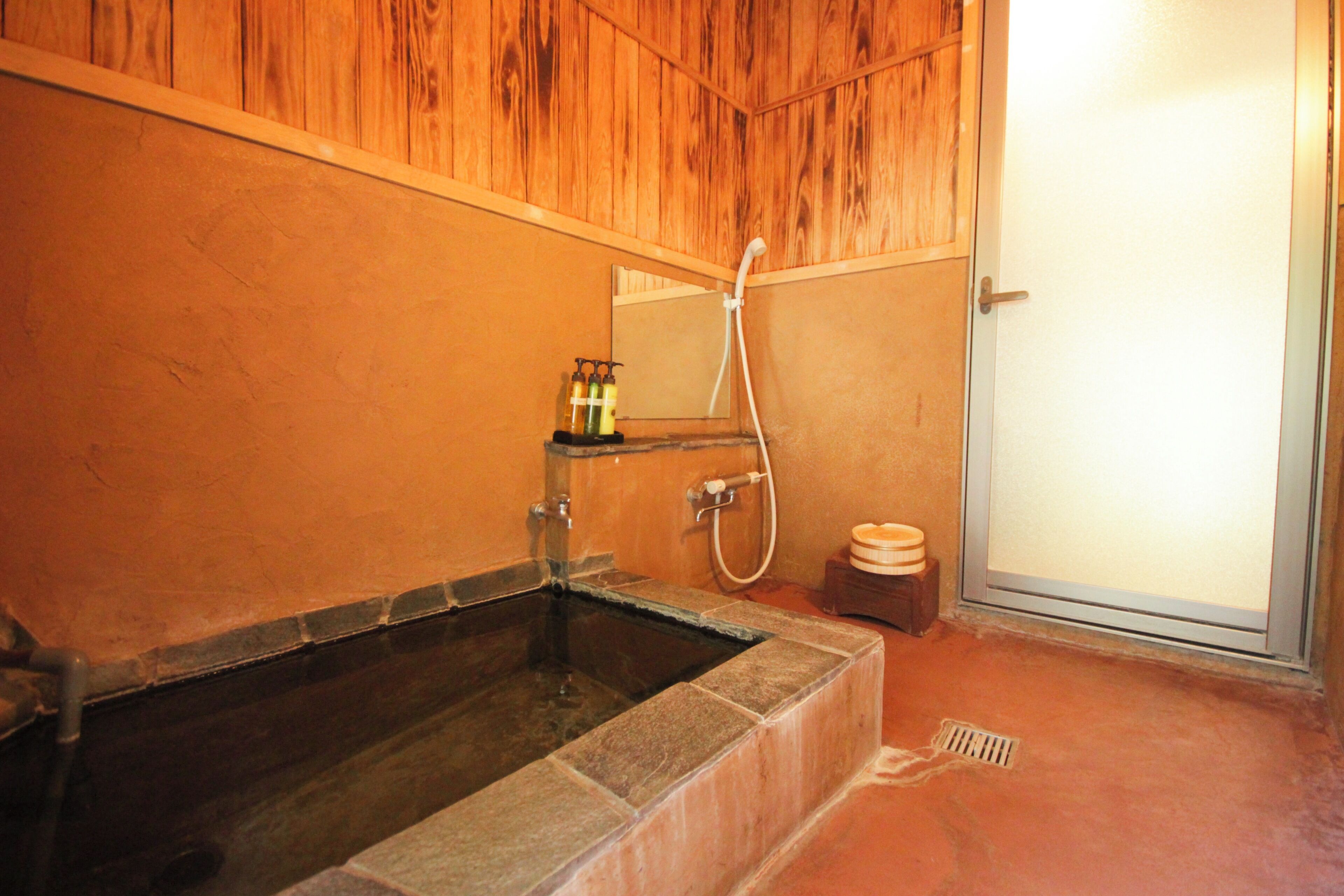 A bathroom with a stone bathtub, wooden paneling, a mirror, and a shower.