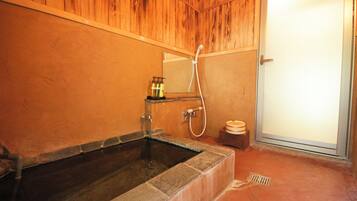 A bathroom with a stone bathtub, wooden paneling, a mirror, and a shower.