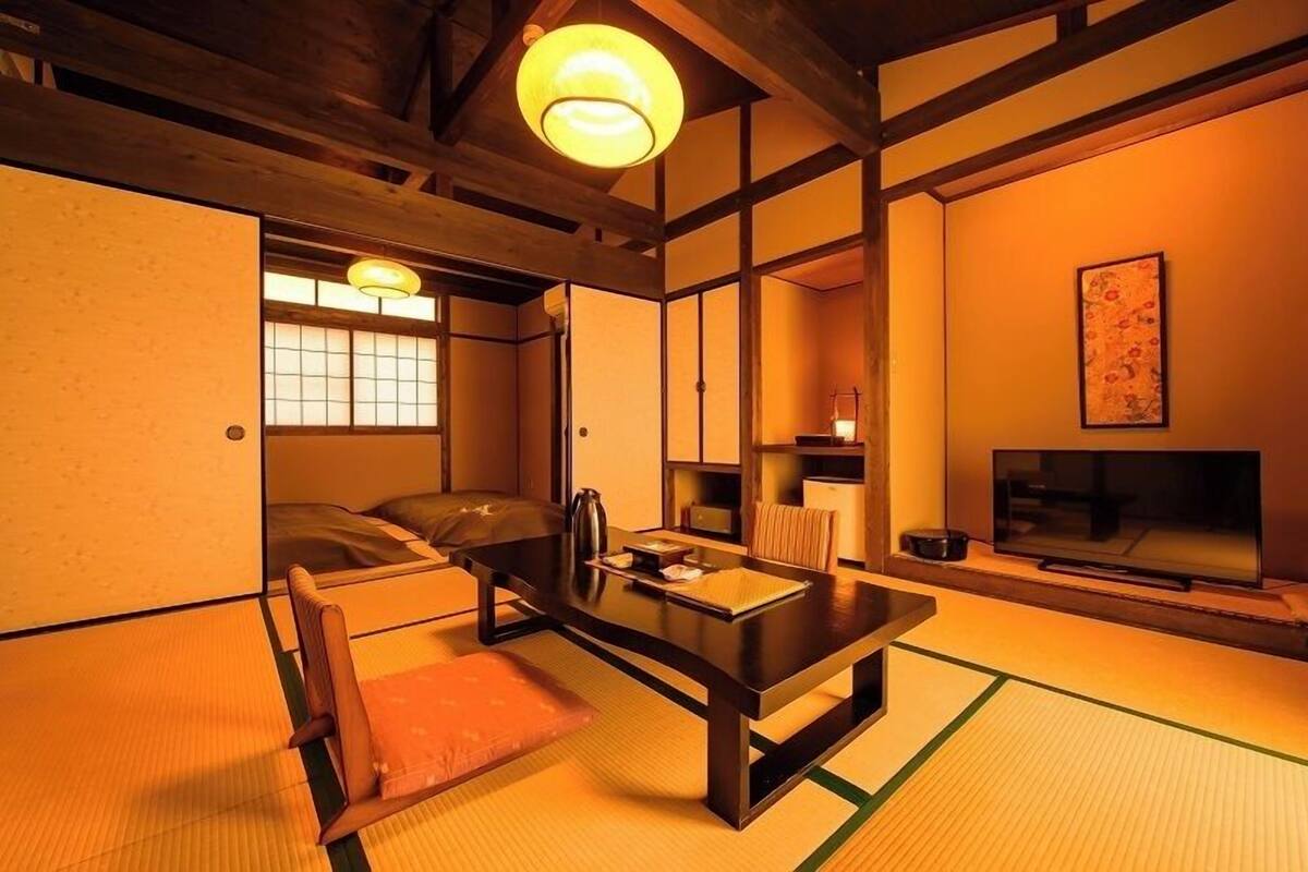 A traditional Japanese-style room with tatami flooring, a low table, a sofa, a television, and a sliding door.