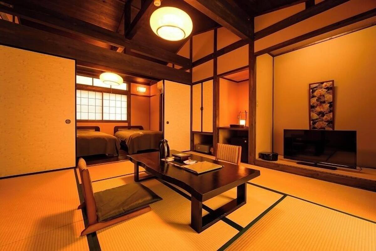 A traditional Japanese room with tatami flooring, a low table, cushions, a television, and sliding doors.