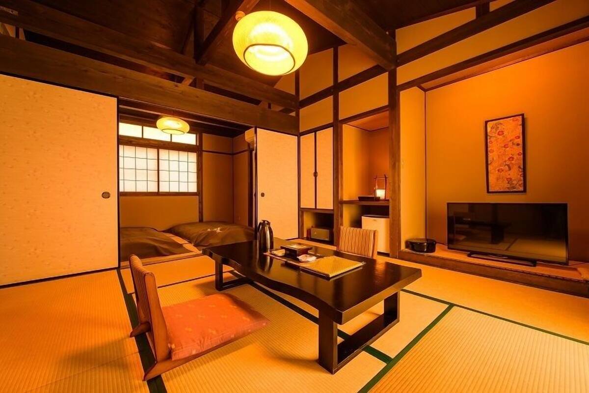 A traditional Japanese room with tatami flooring, a low table, a sofa, a television, and a sliding door.