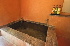 A bathtub with a stone surround, a shelf with toiletries, and a tiled floor. - Yufuin Onsen Yufuin Ryoan Wazanho (Yufu)