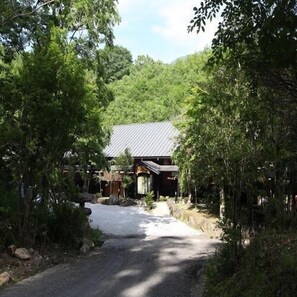 A traditional building with a sloped roof, surrounded by dense greenery and a gravel path leading to it. - Yufuin Onsen Yufuin Ryoan Wazanho (Yufu)