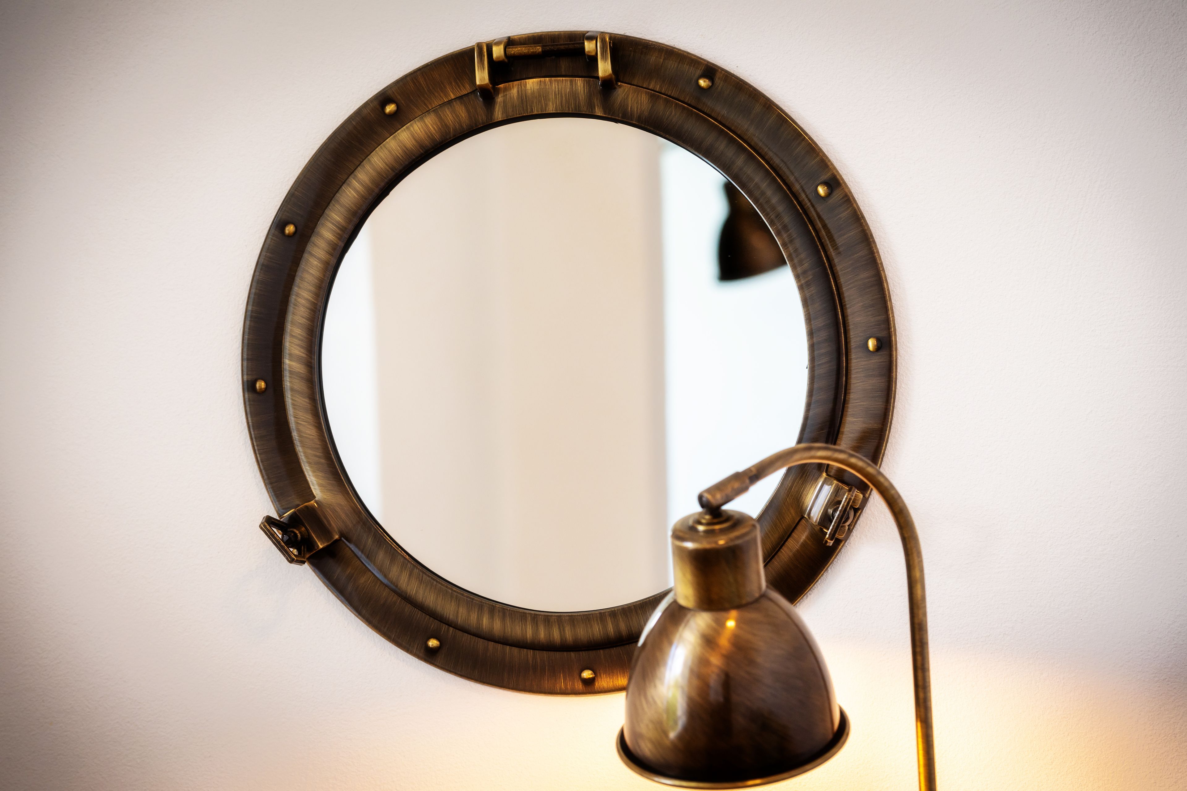 Un miroir rond avec un cadre métallique et une lampe fixée au mur à côté.