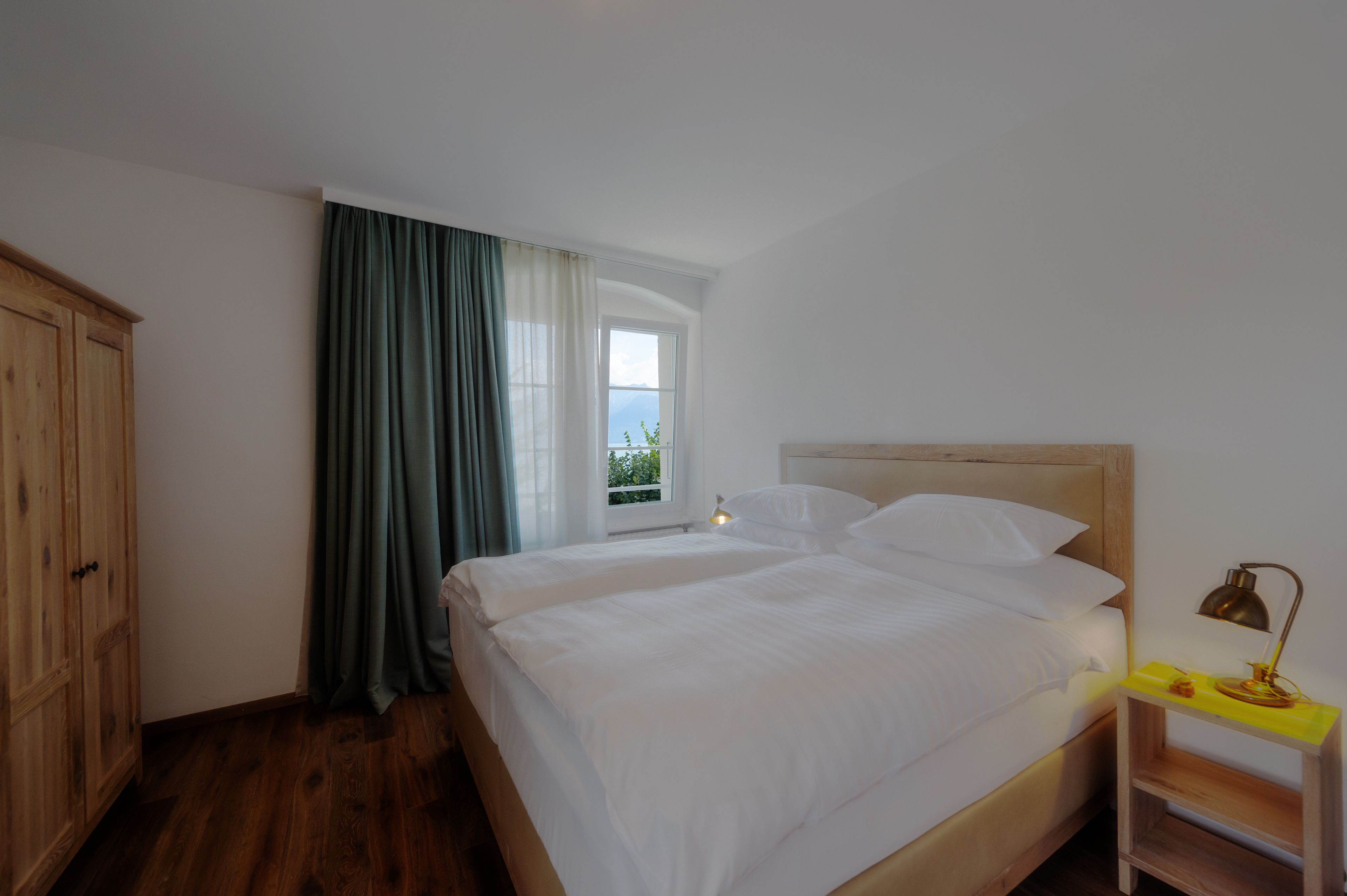 Ein Schlafzimmer mit zwei Betten, einem Holzschrank, einem Fenster mit Vorhängen und einem Nachttisch mit Lampe.