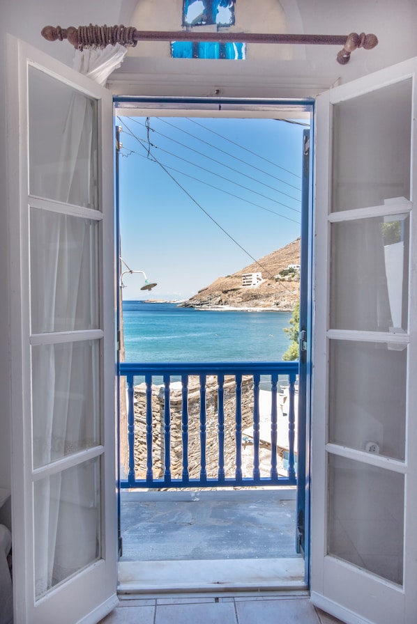 An open door leading to a balcony with a view of a coastal landscape.