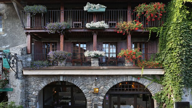A building with a stone facade, wooden balconies with flower boxes, and outdoor seating. - Hôtel Restaurant Le Vieux Logis (Yvoire)