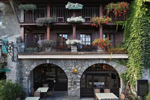 Un edificio con fachada de piedra, balcones de madera con jardineras y asientos al aire libre.