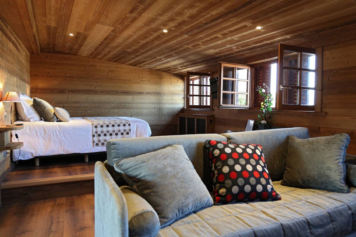 A cozy cabin-style room with a bed, a sofa, and a window with a view.