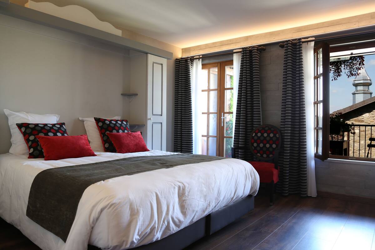 A bedroom with a large bed, a chair, and a view of a building outside.