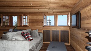 A wooden cabin interior with a sofa, a coffee table, and a TV mounted on the wall. - Hôtel Restaurant Le Vieux Logis (Yvoire)