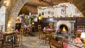 A rustic dining area with wooden tables and chairs, a stone fireplace, and a chandelier. - Hôtel Restaurant Le Vieux Logis (Yvoire)