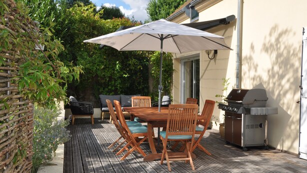 A wooden deck with a table and chairs, a barbecue grill, and an umbrella.