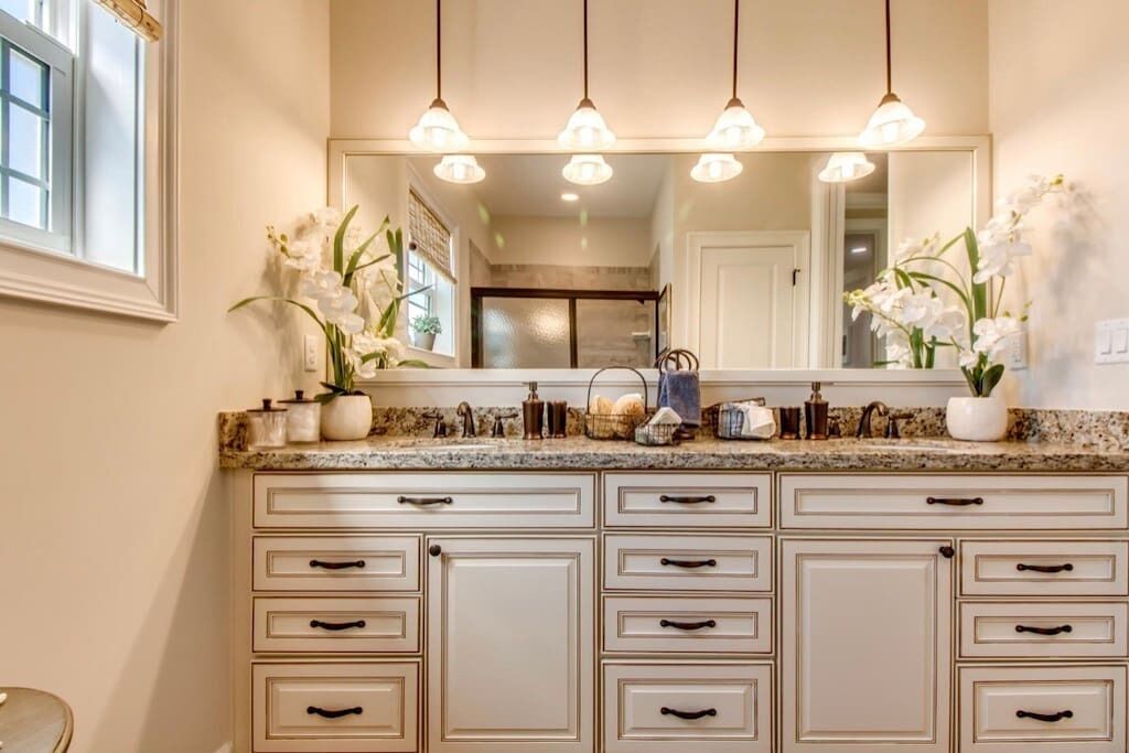 A bathroom with a granite countertop, multiple drawers, a mirror, and white orchids.