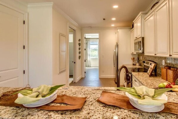 A kitchen with granite countertops, white cabinets, and a stainless steel refrigerator.