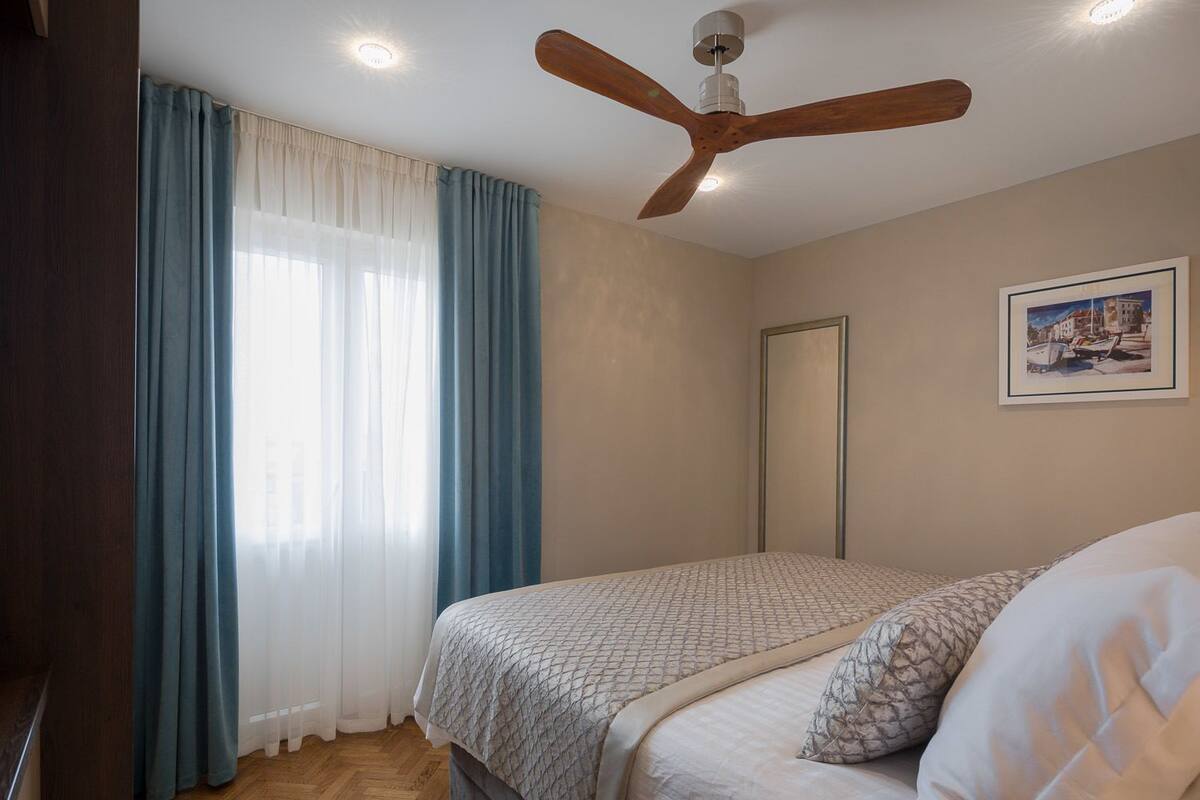 A bedroom with a bed, a ceiling fan, a window with curtains, and a framed picture on the wall.