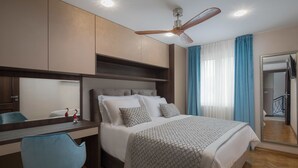 Une chambre d’hôtel moderne dotée d’un grand lit, d’un bureau avec une chaise, d’un ventilateur de plafond et d’un grand miroir.