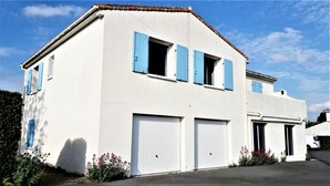 A two-story house with white walls and blue shutters, featuring two garage doors and a small garden with flowers.