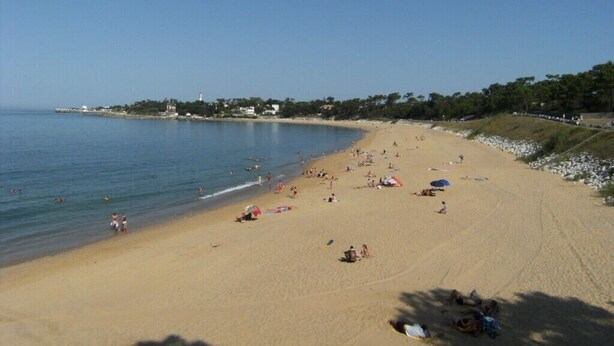 A wide sandy beach with clear blue water, umbrellas, and people relaxing.