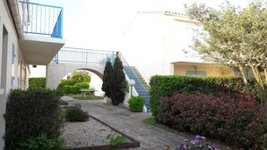 A courtyard with a stone pathway, a small table, and a staircase leading to a building with a blue railing.