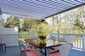 Une terrasse extérieure couverte, avec une table en verre, des chaises blanches et un vase rempli de fleurs jaunes.