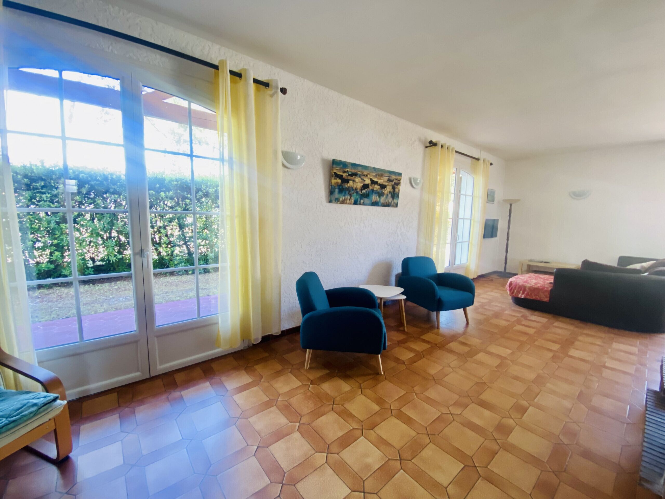 A spacious living room with a large sliding glass door leading to a patio, two blue armchairs, a small white table, and a black sofa.