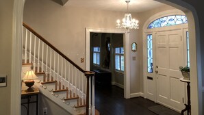A hallway with a wooden staircase, a chandelier, a white door with stained glass, and a potted plant. - Kentucky at its best! Historical meets modern amenities! (Louisville)