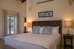 A bedroom with a bed, two bedside lamps, a wall-mounted sign, and a door with curtains.